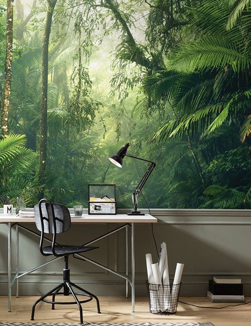 Ein Schreibtisch mit Stuhl steht vor einer tapezierten Wand auf der eine Fotodruck von Dschungelpflanzen zu sehen ist