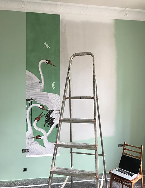 Leiter steht vor Wand mit einer Bahn von mintfarbener Vintage-Tapete mit Kranichen